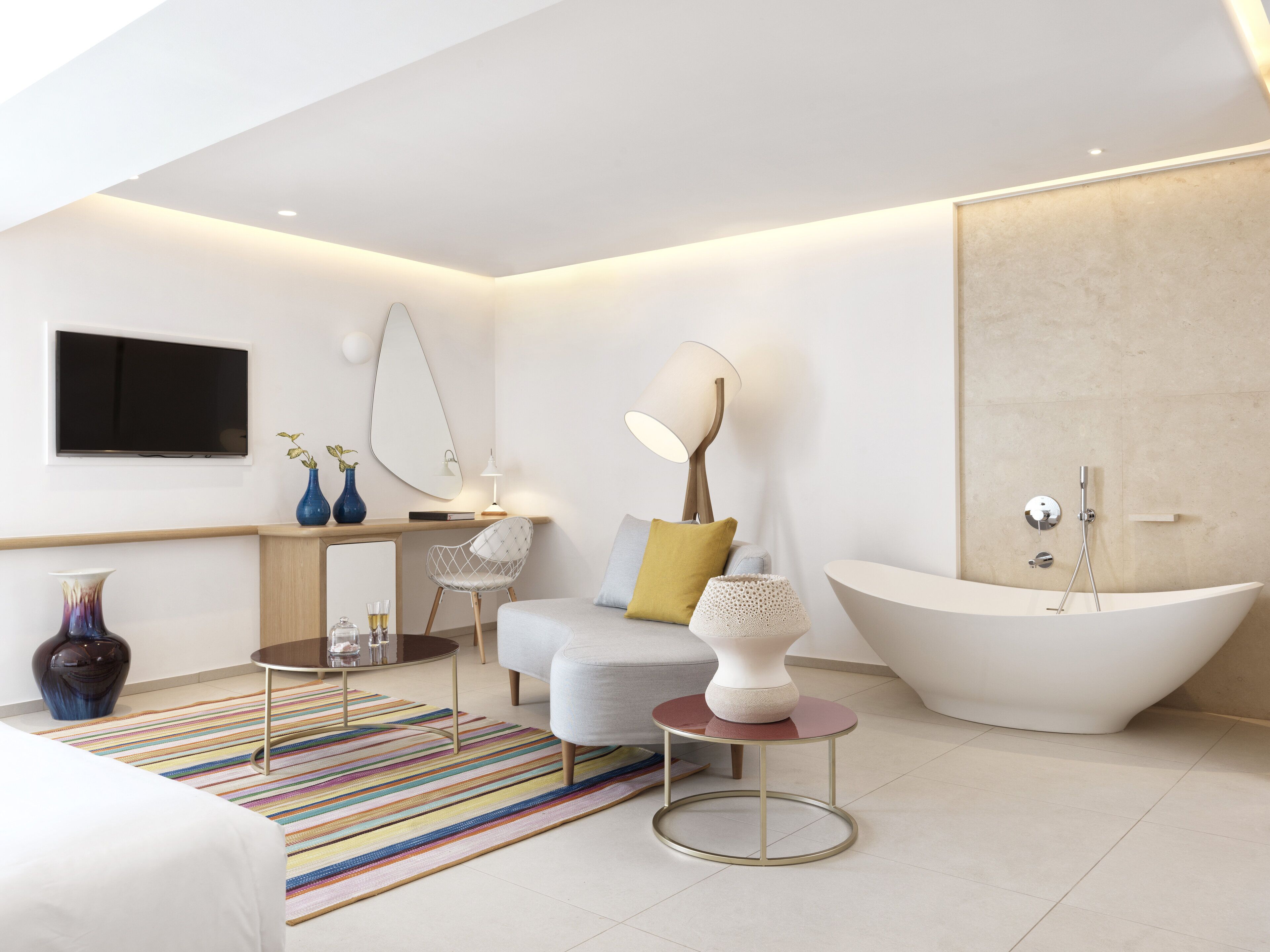 A modern bathroom with a freestanding bathtub, a sofa, a coffee table, and a TV mounted on the wall.