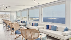Una habitación moderna y amplia con un sofá blanco, sillas de mimbre y ventanas grandes que dan al mar.