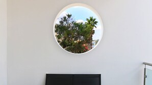 Ein runder Spiegel an einer weißen Wand, mit Blick auf Bäume und ein Gebäude.