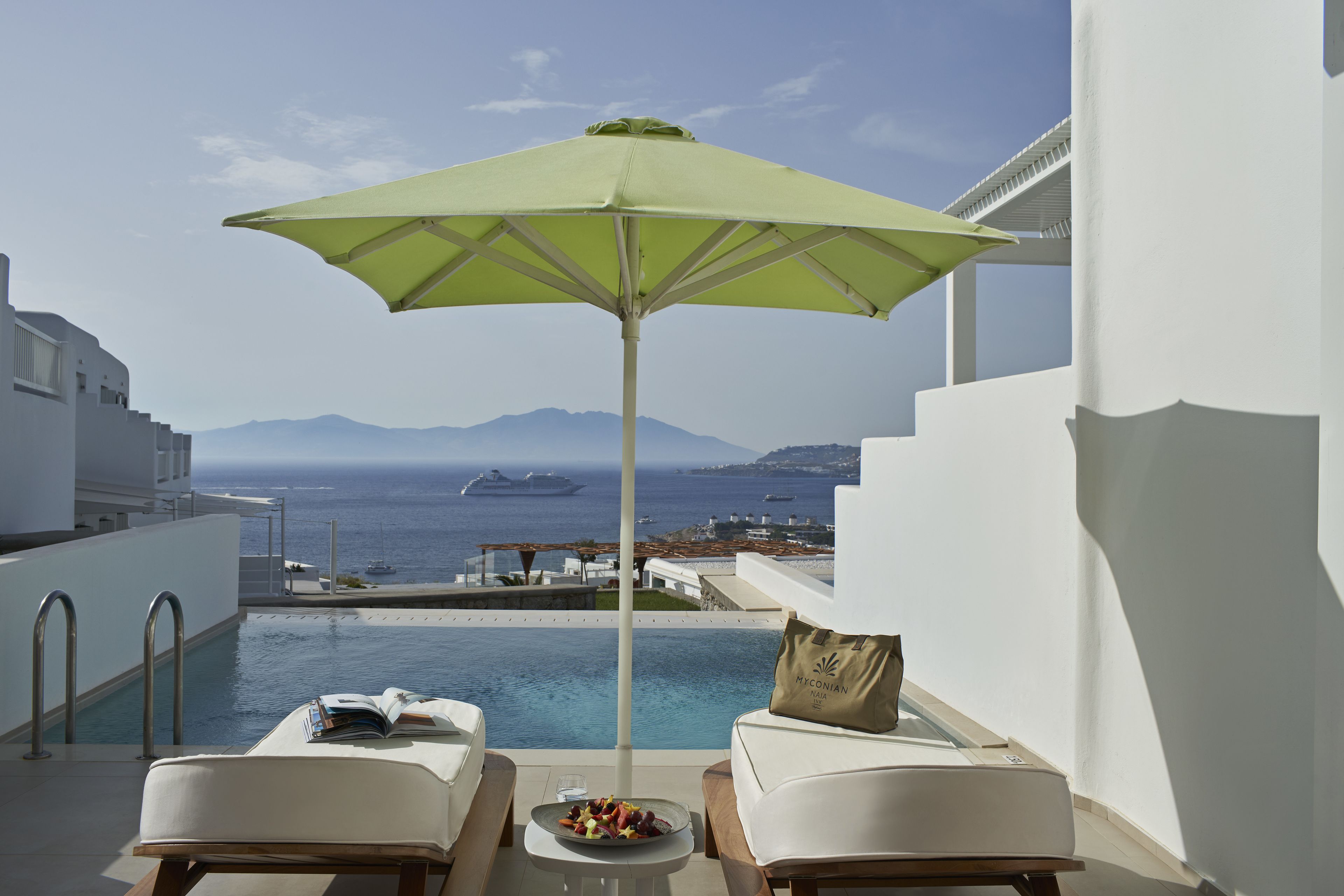 A poolside area with two lounge chairs, a table with a bowl of fruit, and a green umbrella.