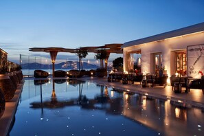 Uma área de piscina tranquila com vista desimpedida para as montanhas, assentos modernos ao ar livre e um edifício bem iluminado.