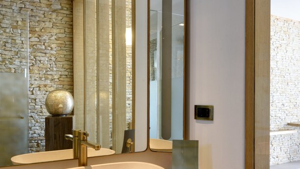 Une salle de bain moderne avec un grand miroir, un mur en pierre et un meuble-lavabo en bois.