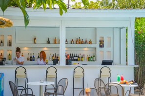 A bar area with multiple shelves of bottles, a counter with a person, and several chairs and tables.