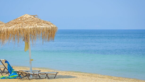A beach with a straw umbrella and lounge chairs.
