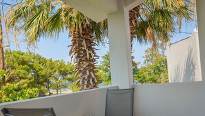 A balcony with a table and chairs, palm trees, and a view of the beach.