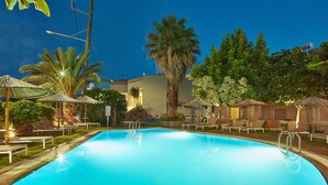 A swimming pool with lounge chairs and umbrellas, surrounded by palm trees and a building.