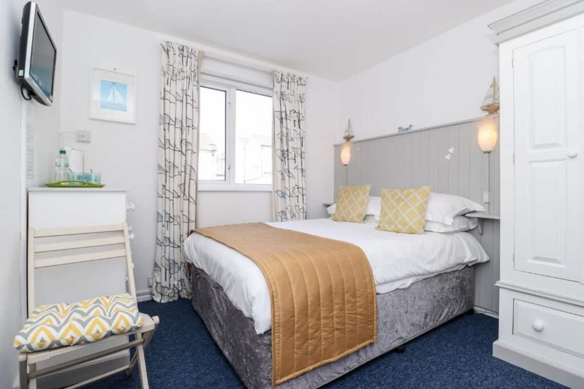 A bedroom with a bed, a bedside table, a chair, a wardrobe, a television, and a window with curtains.
