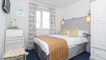 Un dormitorio con cama, mesita de noche, una silla, armario, televisor y ventana con cortinas.