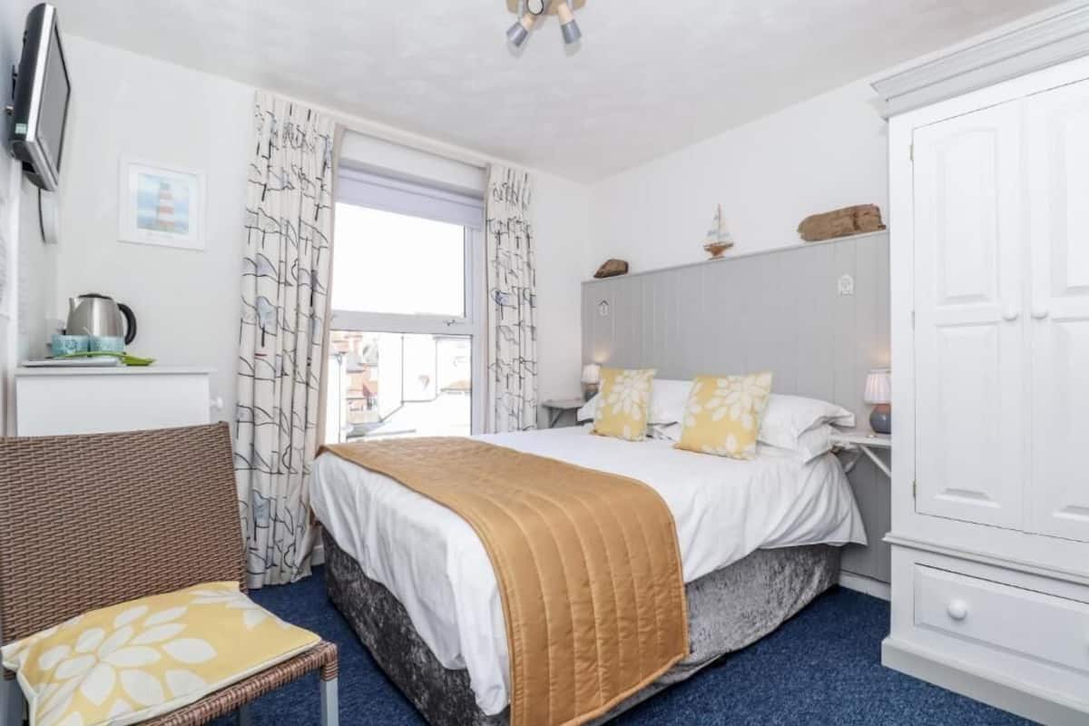 A bedroom with a bed, a chair, a wardrobe, and a window with curtains.