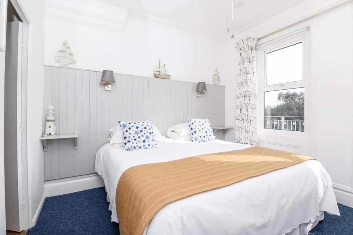 A bedroom with a bed, white bedding, a blue carpet, and a window with a view.