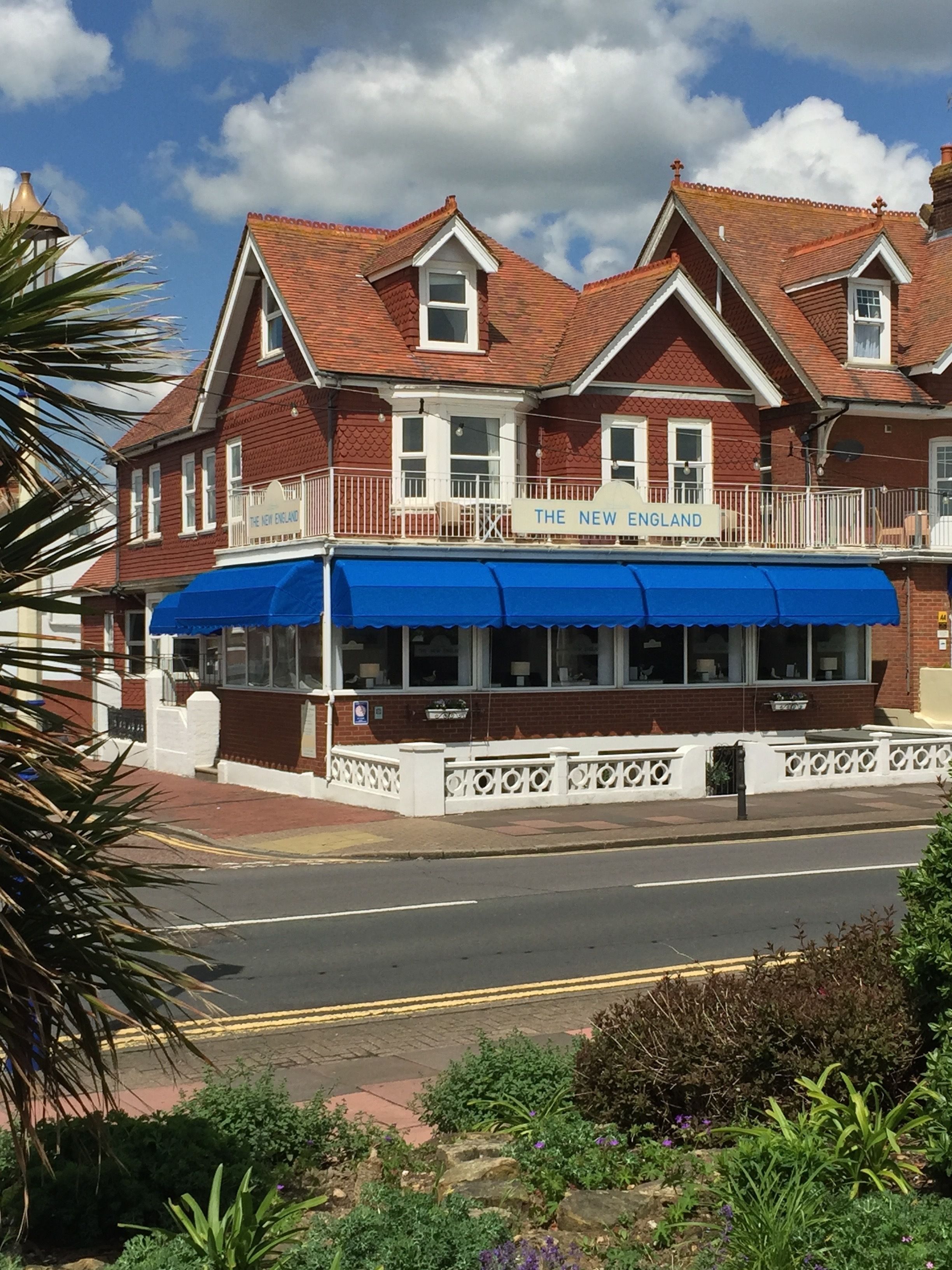 Un bâtiment à deux étages, avec une façade en briques rouges, un auvent bleu et une enseigne indiquant « The New England ».