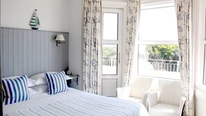 A bedroom with a bed, a nightstand, a lamp, a chair, and a window with curtains. - The New England (Eastbourne)