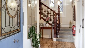 A staircase with a wooden handrail and a floral arrangement at the bottom. - The New England (Eastbourne)