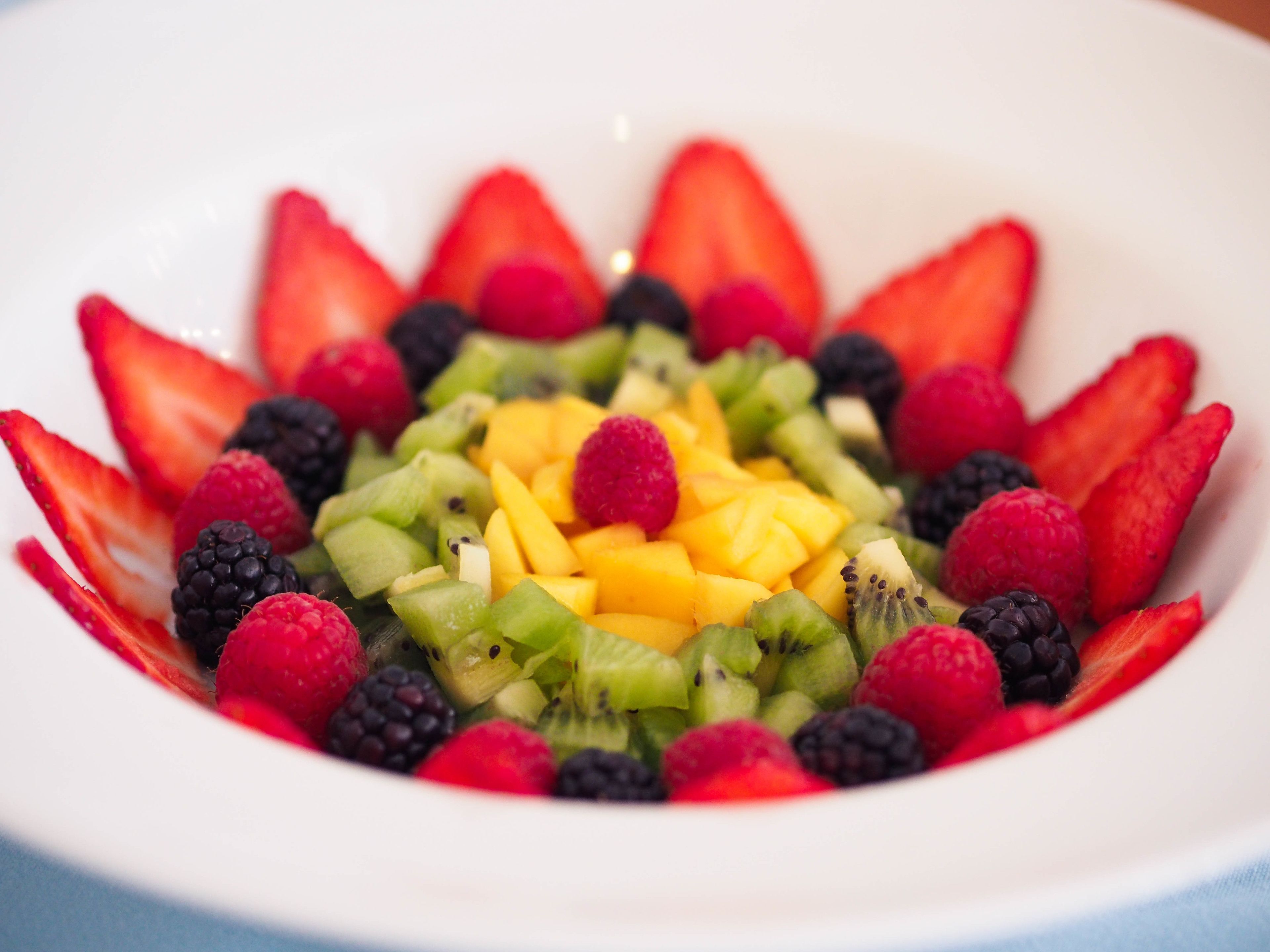 A bowl of mixed fruit salad with strawberries, raspberries, blackberries, kiwi, and mango.