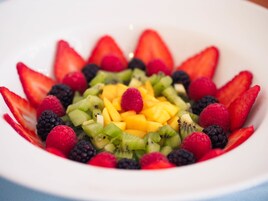 A bowl of mixed fruit salad with strawberries, raspberries, blackberries, kiwi, and mango.