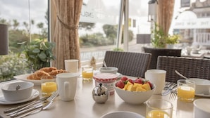A breakfast setting with croissants, fruit, and beverages on a table with wicker chairs and a view of the city. - The New England (Eastbourne)