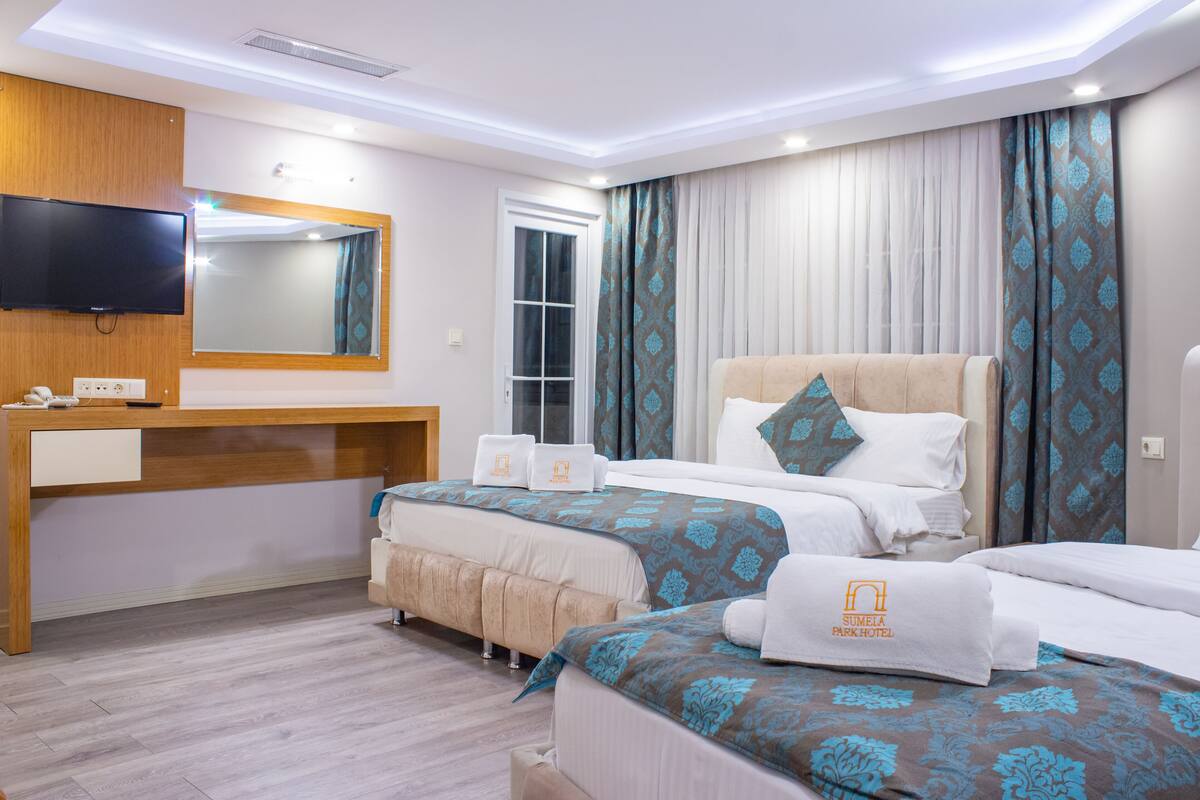 A hotel room with two beds, a TV, a desk, and a large window with curtains.