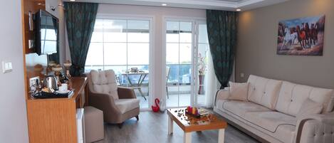 A living room with a sofa, a coffee table, a TV, and a balcony with a view.