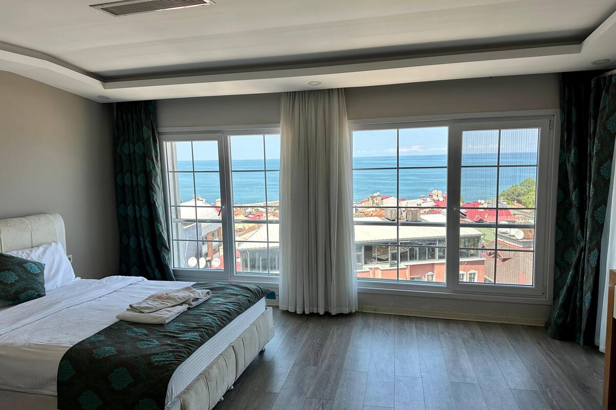 A hotel room with a large window offering a view of the sea and cityscape.