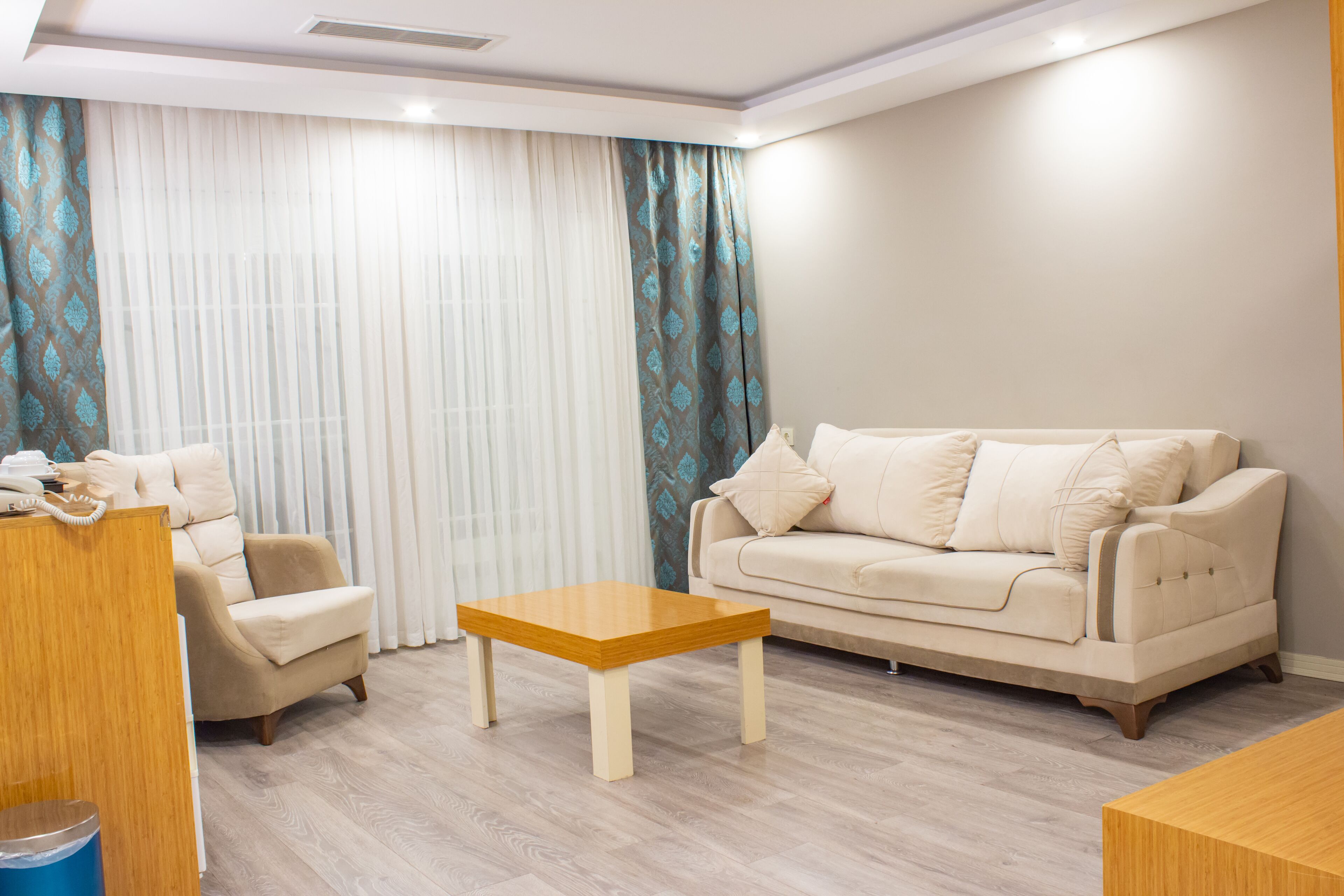 A living room with a beige sofa, a wooden coffee table, and a patterned curtain.