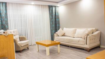 A living room with a beige sofa, a wooden coffee table, and a patterned curtain.