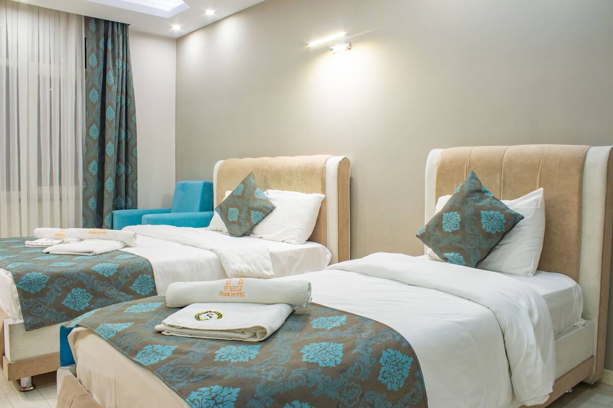 A hotel room with two beds, each with a headboard, a blue chair, and a large window with curtains.