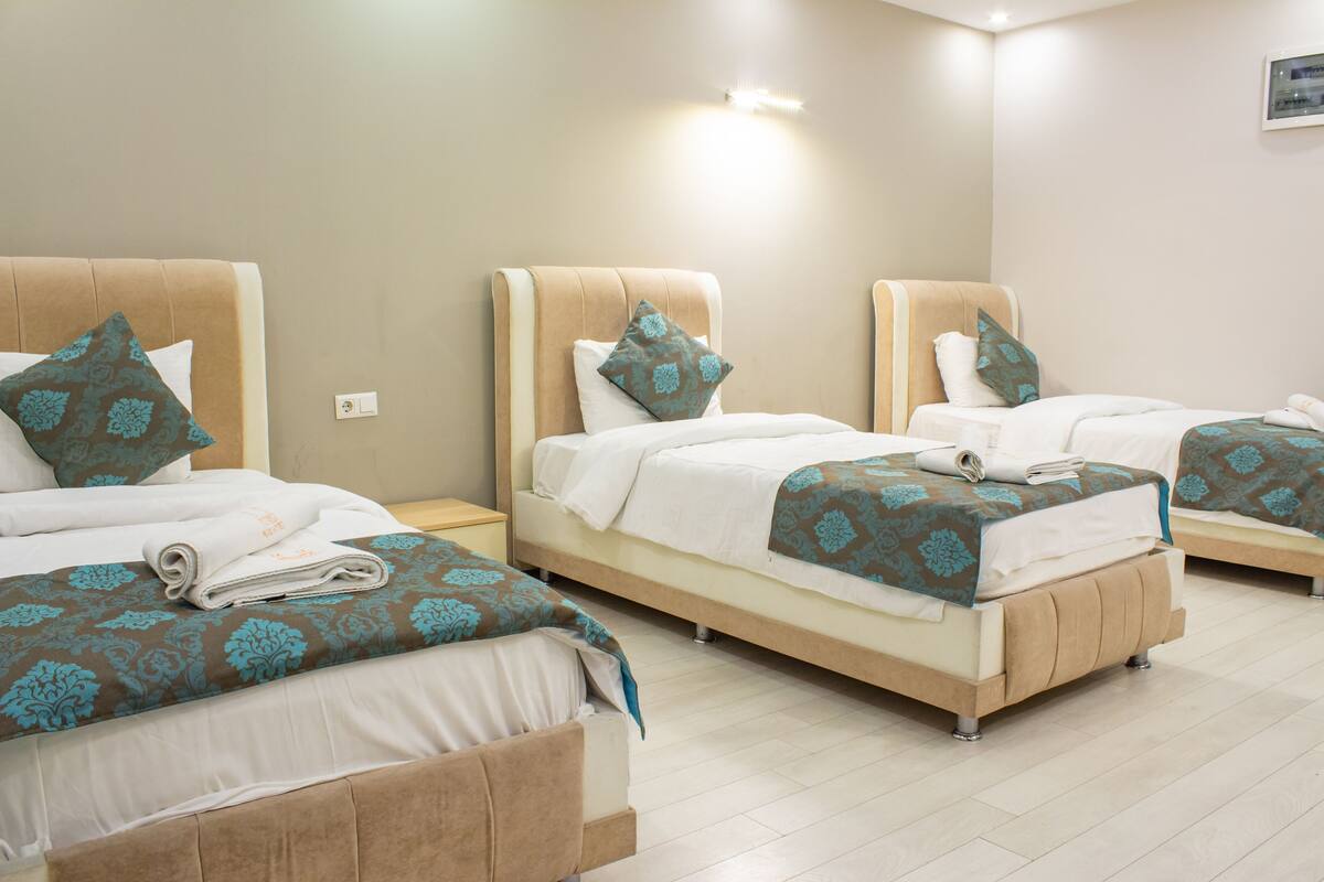 A hotel room with three beds, each with a headboard, white bedding, and a teal patterned throw.