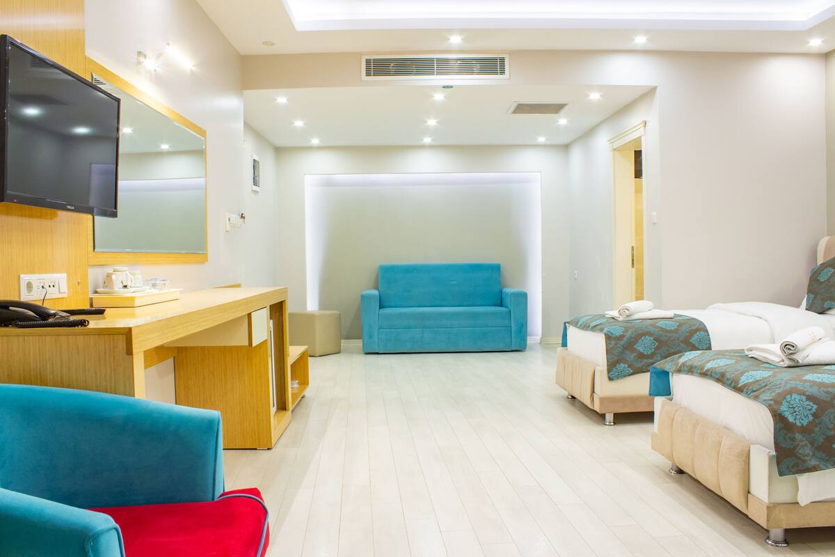 A hotel room with a desk, two beds, a TV, and a large window.