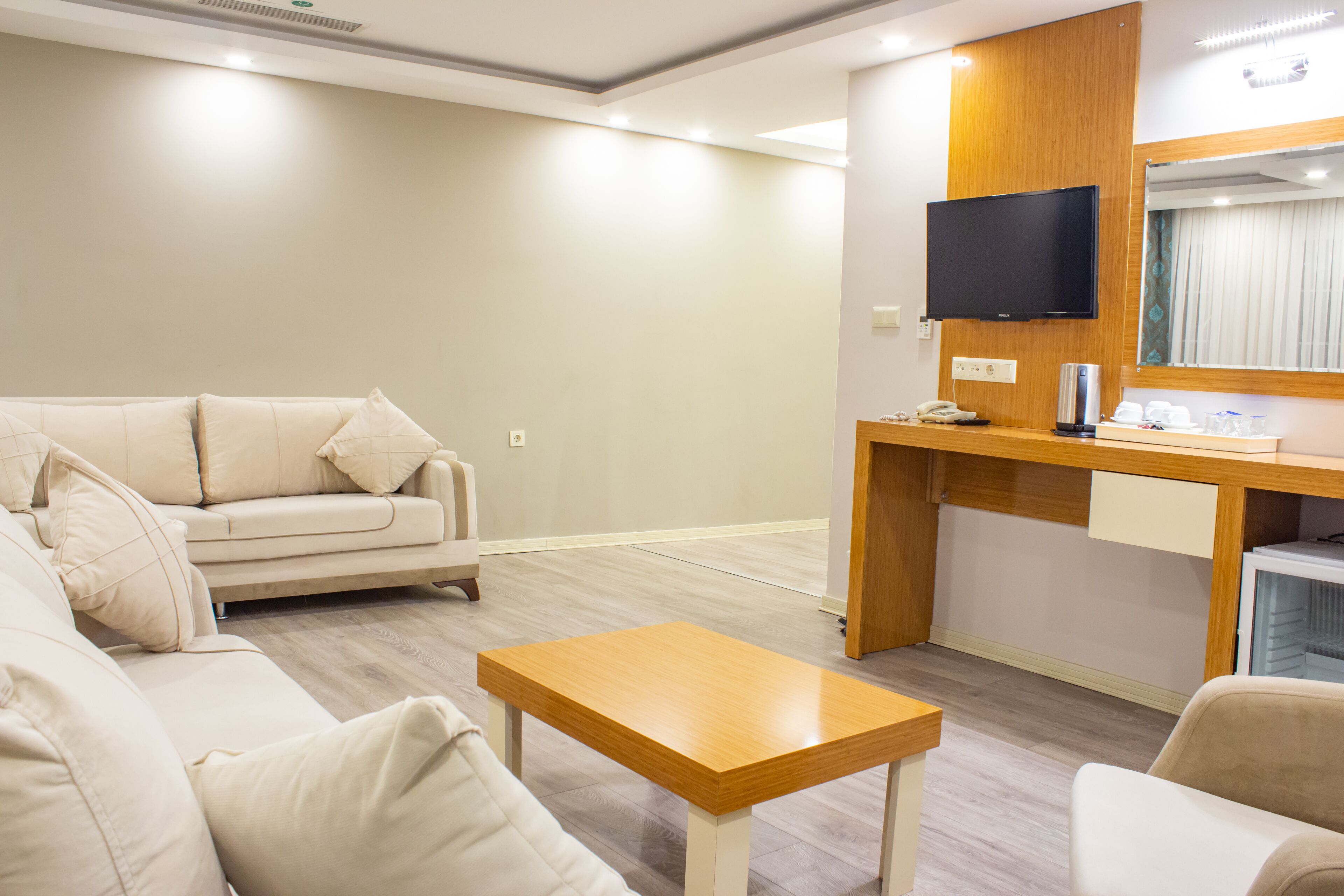 Uma sala de estar moderna com um sofá bege, uma mesa de centro de madeira e uma TV de tela plana fixada em um painel de madeira.