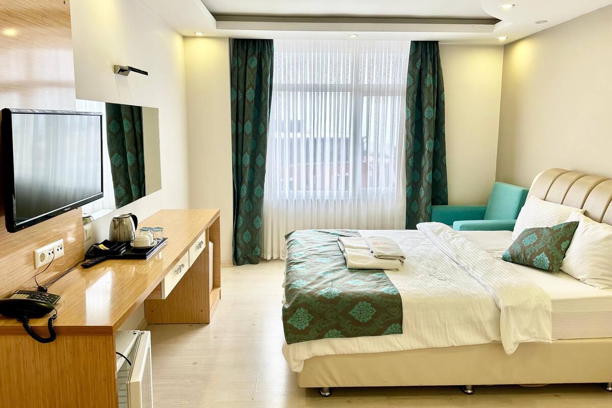 A modern hotel room with a bed, a desk with a television, and a window with curtains.