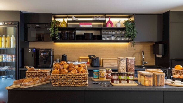 A modern kitchen with a central island stocked with bread, pastries, and condiments. - Korner Sorbonne (Paris)