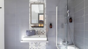 A bathroom with a white sink, a mirror, a shower, and patterned tiles. - Korner Sorbonne (Paris)
