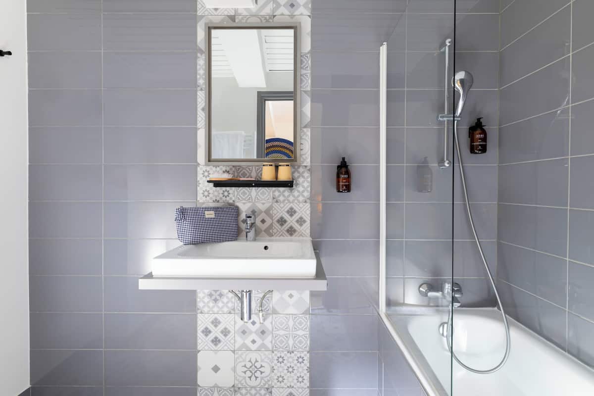 A bathroom with a white sink, a mirror, a shower, and patterned tiles.