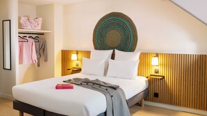 A modern bedroom with a bed, bedside lamps, a wooden headboard, and a wall-mounted decorative item. - Korner Sorbonne (Paris)