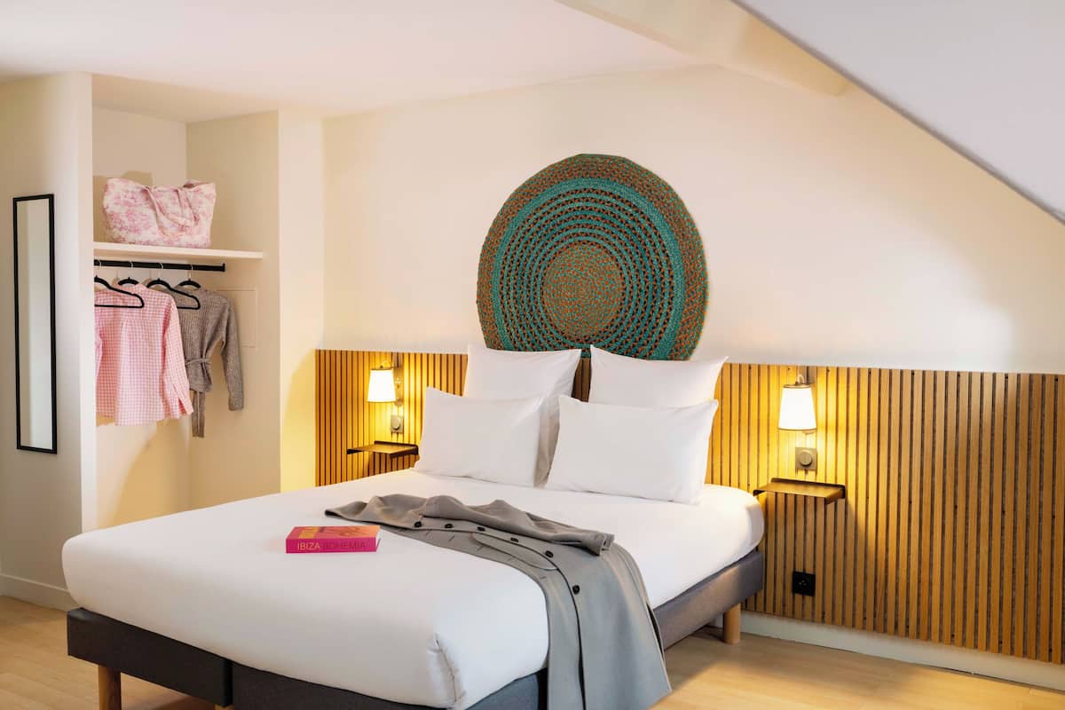 A modern bedroom with a bed, bedside lamps, a wooden headboard, and a wall-mounted decorative item.