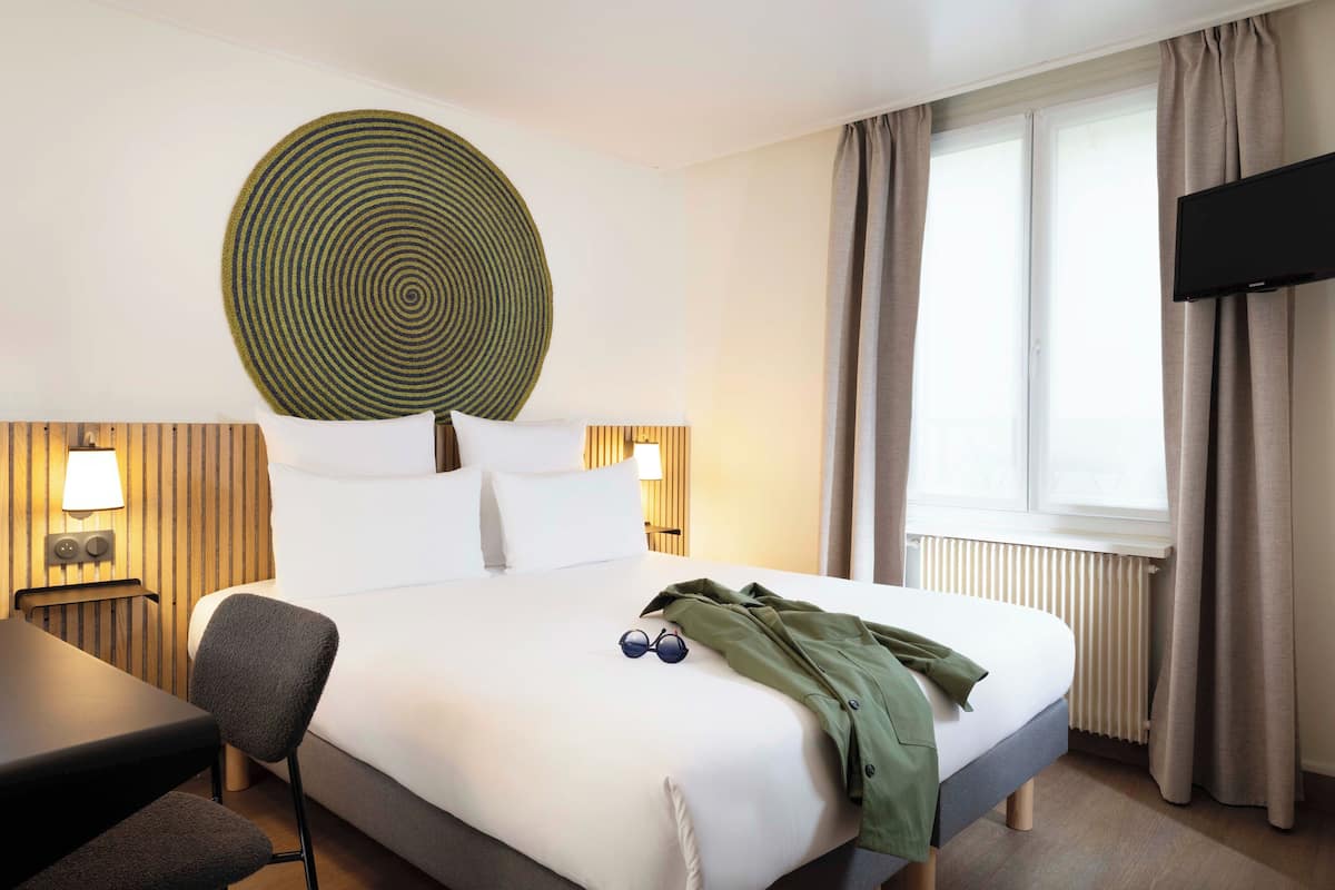 A hotel room with a bed, a desk, a chair, a television, and a window with curtains.