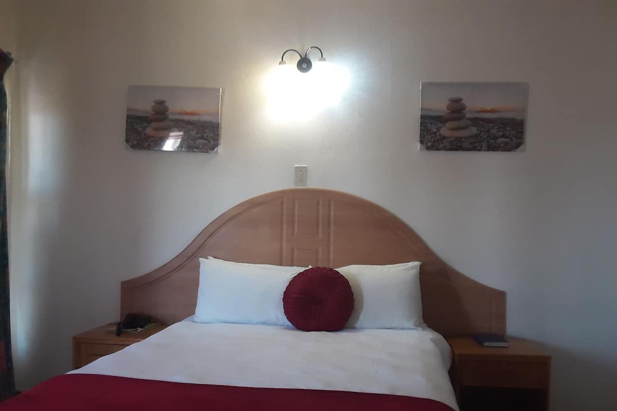 Une chambre d’hôtel comprenant un lit, deux tables de chevet, une lampe fixée au mur et deux tableaux encadrés.