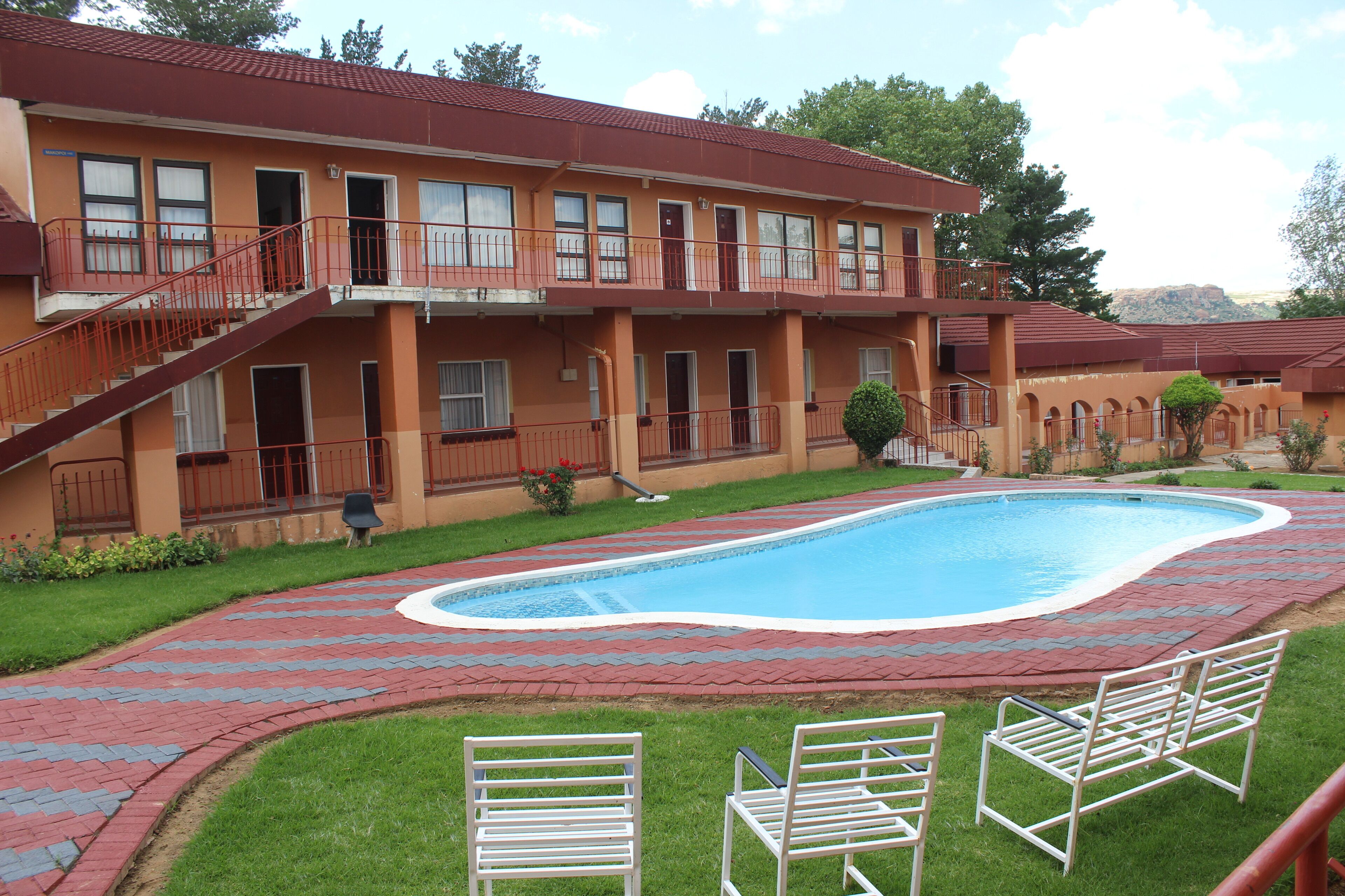 A hotel with a swimming pool, a covered patio, and a two-story building with balconies.