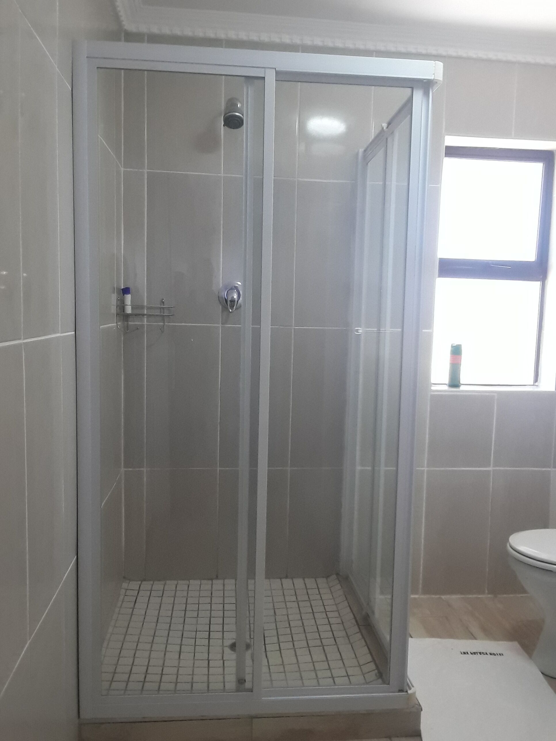 A walk-in shower with a glass door, tiled walls, and a window above the toilet.