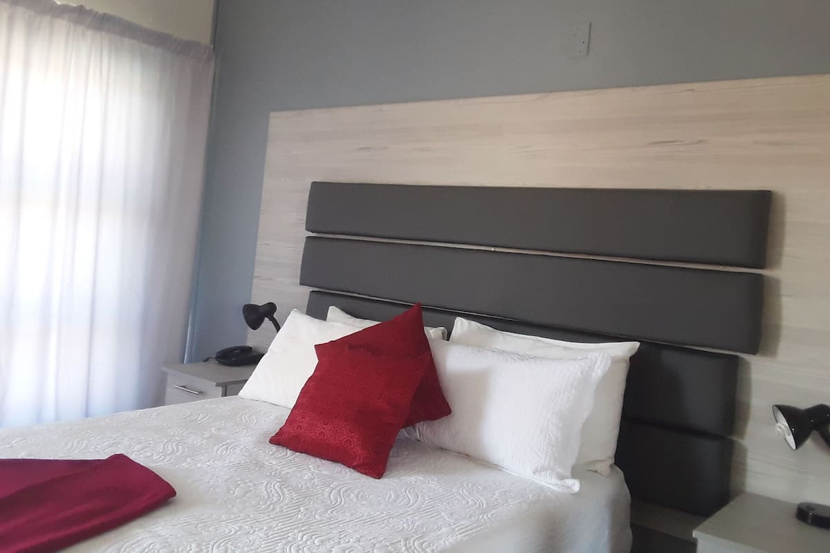 Une chambre d’hôtel avec un grand lit, une tête de lit, deux tables de chevet et une petite table d’appoint.