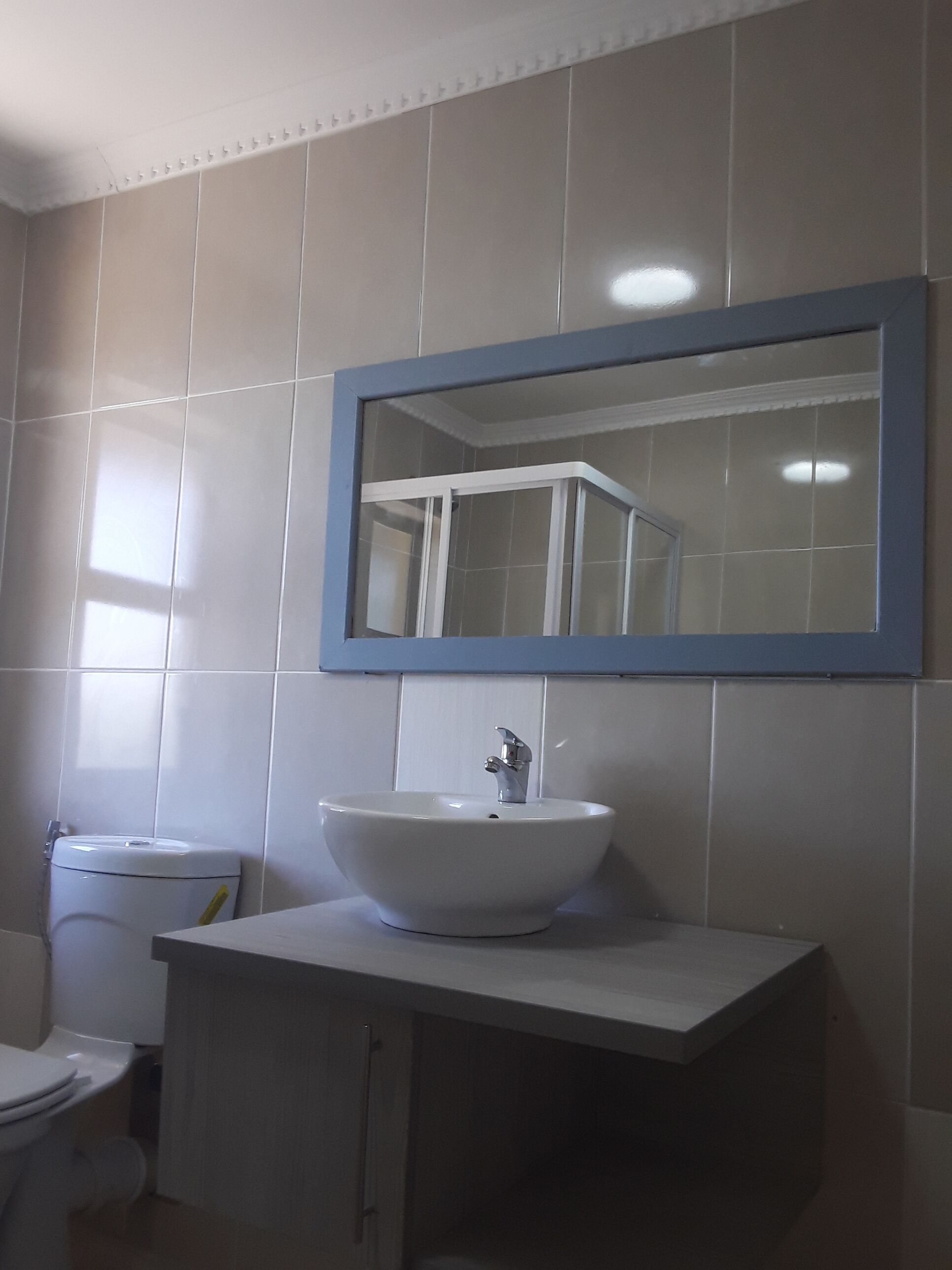 Ein Badezimmer mit einem weißen Waschbecken, einem Spiegel darüber und einer Toilette links.