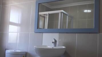 Ein Badezimmer mit einem weißen Waschbecken, einem Spiegel darüber und einer Toilette links.