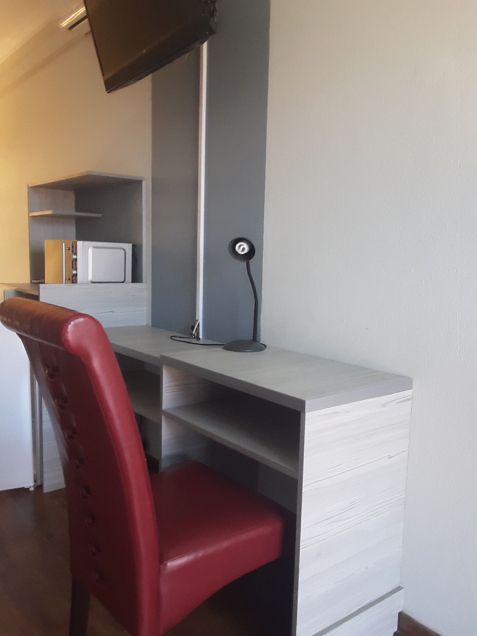 A compact kitchen with a microwave, a red chair, and a desk with a lamp.