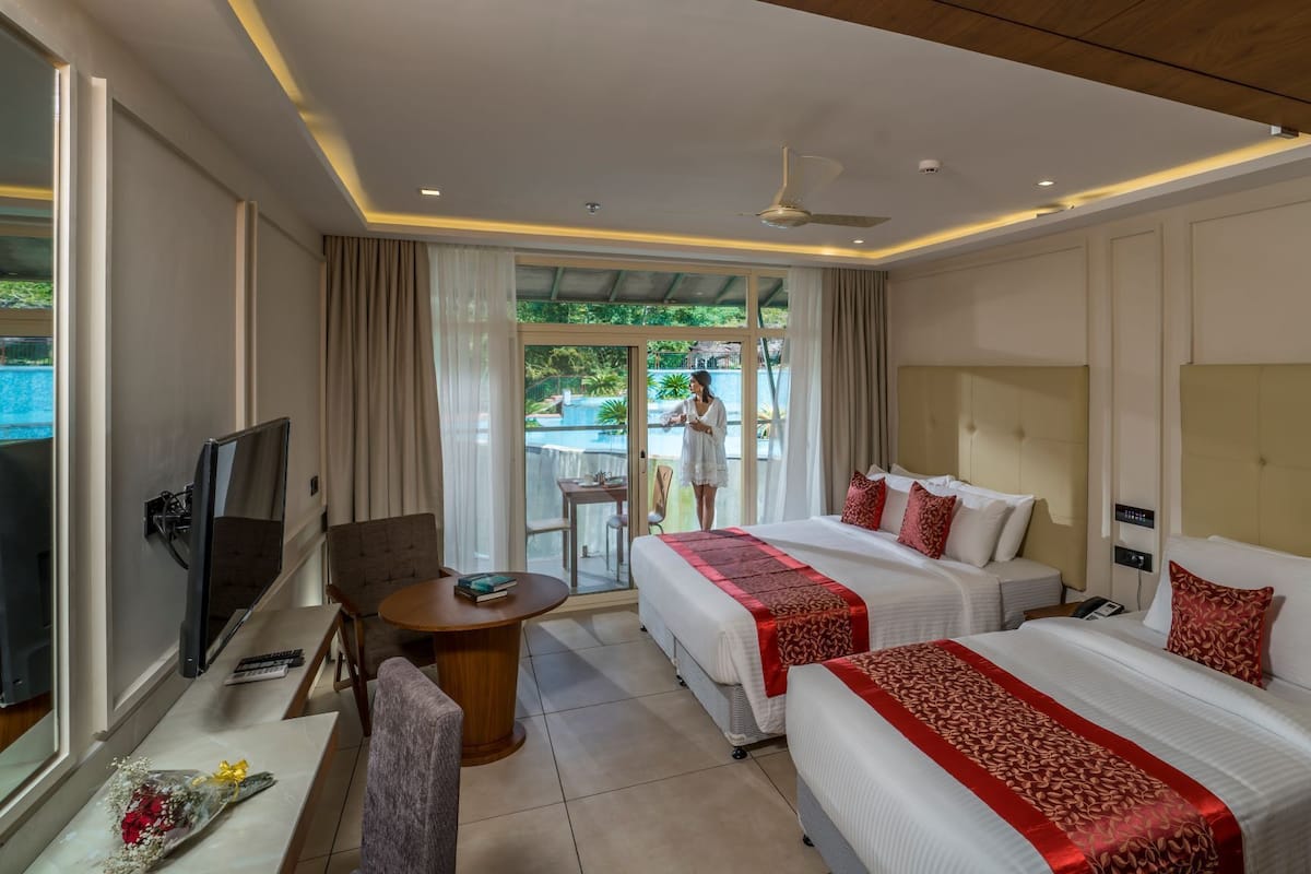 Habitación de hotel con dos camas, televisión, escritorio y vista a una piscina al aire libre.
