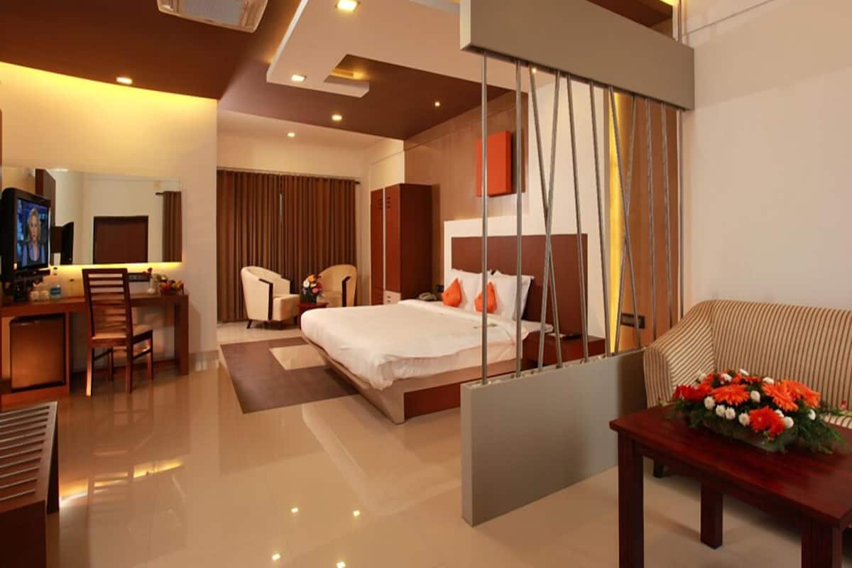 Una habitación de hotel moderna con una cama, un escritorio con computadora, un televisor y una zona de estar con sofá y mesa.