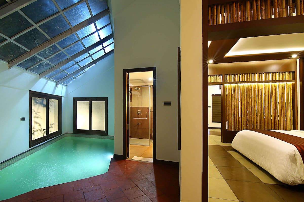 Habitación de hotel con una cama grande, baño y zona de piscina con techo de cristal.