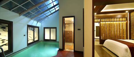 Habitación de hotel con una cama grande, baño y zona de piscina con techo de cristal.
