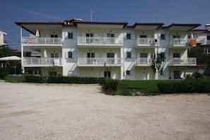 A multi-story building with balconies, a sign indicating a business, and a gravel driveway. - Pavloudis Apartments (Polygyros)