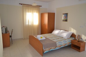 A bedroom with a bed, a wardrobe, a desk with a computer, and a nightstand with a lamp. - Pavloudis Apartments (Polygyros)
