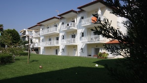 A multi-story hotel with balconies, a well-maintained lawn, and a clear sky. - Pavloudis Apartments (Polygyros)